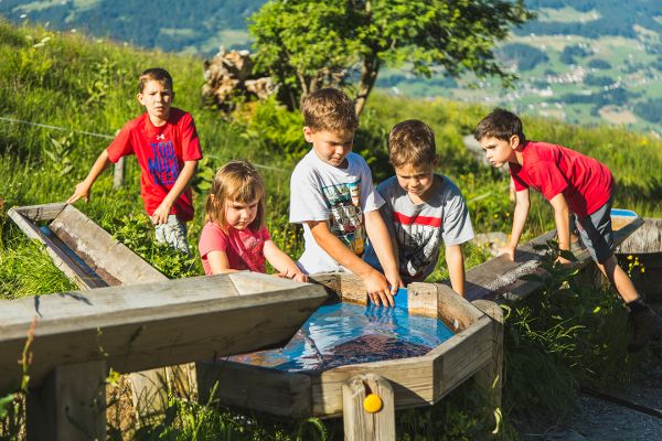 Fünf Kinder stehen an einer Wasserstelle und spielen mit dem Wasser.