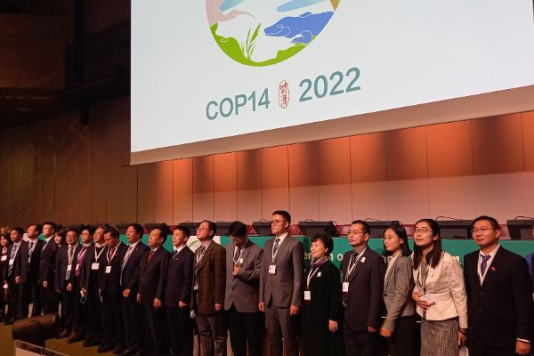 asiatische Teilnehmerinnen und Teilnehmer der COP 14 stehen nebeneinander im Hintergrund das Logo und die Aufschrift COP 14 2022 
