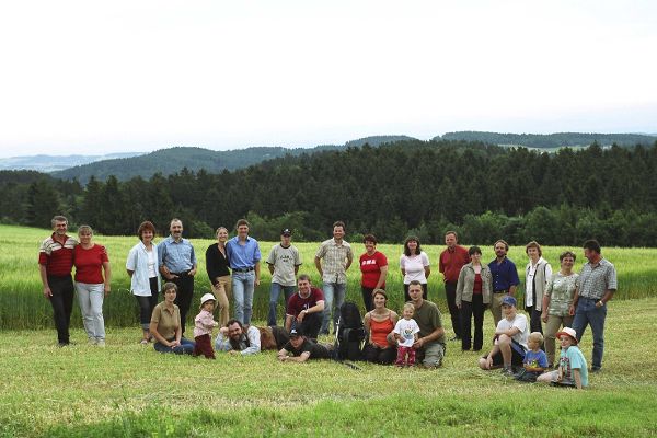 Gruppen Menschen auf einer grünen Wiese, im Hintergrund eine bewaldete Hügelkette