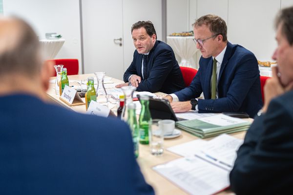 Landwirtschaftsminister Totschnig und Landesrat Ganter sitzen an einem Tisch auf dem sich Unterlagen und Wasserflaschen befinden, am Bildrand sind zwei Männer in Rückansicht erkennbar