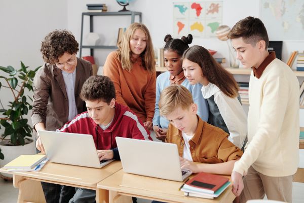 Eine Lehrerin zeigt einer Gruppe von Teenagern Lehrinhalte auf zwei Laptops