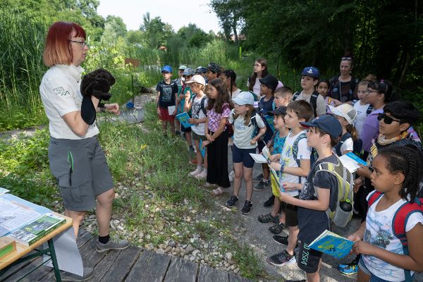 Eine Nationalpark-Rangerin mit einer Biberfigur auf der Hand spricht zu Schülerinnen und Schüler vor dem Stand zu 40 Jahre Ramsar 