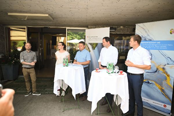 Vertreterinnen und Vertreter des Bundesministeriums für Wasserwirtschaft und der Wasserwirtschaft des Landes Oberösterreich stehen beim Pressetermin, vor ihnen zwei Stehtische, im Hintergrund Rollups der jeweiligen Institutionen